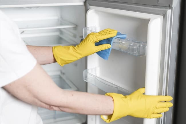 Personne netooyant un bac de frigidaire avec des gants jaunes.