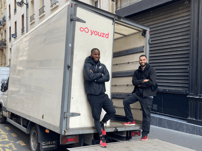 Deux livreurs photographiés devant un camion blanc dans une rue.