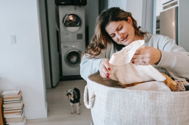 Une femme plie du linge avec un lave-linge et un sèche-linge en arrière plan