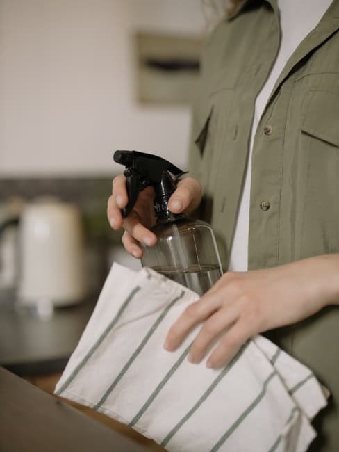 Personne nettoyant une surface avec un chiffon et du vinaigre, méthode plus durable et écologique que d'utiliser des produits chimiques.